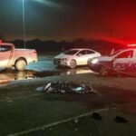 Corpo no chão coberto e carros de polícia ao redor