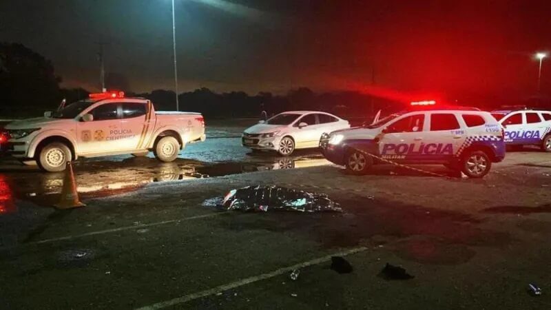 Corpo no chão coberto e carros de polícia ao redor